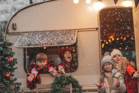 Téléchargez les photos : Enfants célébrant Noël et Nouvel An saison des fêtes d'hiver en plein air attendant le Père Noël. Enfants joyeux passer du temps ensemble près de caravane camping-car de Noël se réjouit à la première neige profiter de l'enfance - en image libre de droit