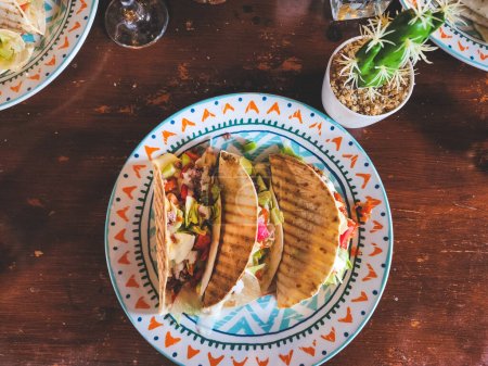 Foto de Vista de arriba hacia abajo de los tacos gourmet de inspiración mexicana de Bulgaria. carne de res, pepino, tomate, lechuga, pimientos y salsa roja. sobre mesa de madera - Imagen libre de derechos