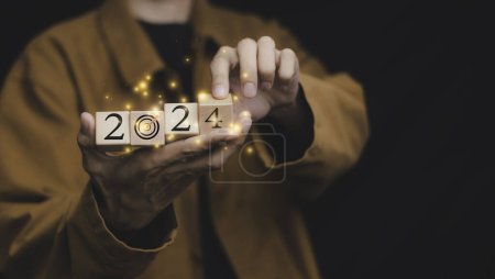 Téléchargez les photos : Businessman holding a wooden block. Dart board, conceptualization to lead to the right goal. cube block to contain the purpose of doing business overcoming. Developing ideas for the new year 2024. - en image libre de droit