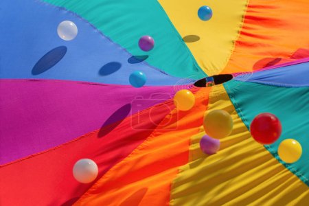 Foto de Multicolor-patterned kids play parachute with colorful bouncing balls. Rainbow colors toys for outdoor activities - Imagen libre de derechos