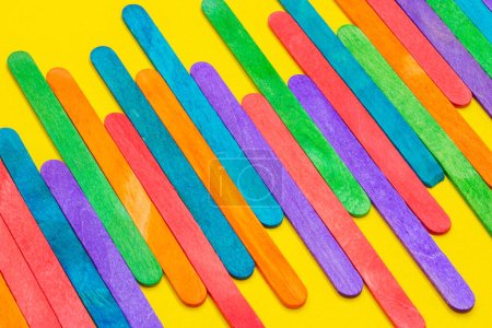 Photo for Colored popsicle sticks arranged side by side. Wooden ice cream sticks on yellow paper. Multicolored background - Royalty Free Image