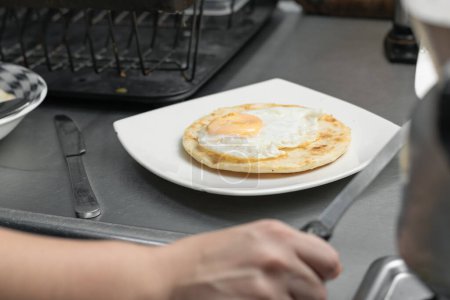 Foto de Típico desayuno colombiano servido en un plato blanco encima de un plato de metal. arepa con huevos y huevos pequeños para comer. - Imagen libre de derechos