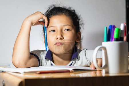 Foto de Little girl, latina student doing her homework very thoughtful and distracted looking the other way - Imagen libre de derechos