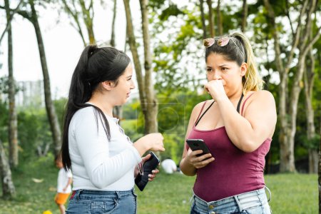 Photo for Latina girls taking a walk in the park while talking with their cell phone in hand - Royalty Free Image