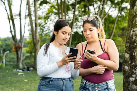 girl showing her friend the text messages she has on her cell phone while taking a walk in the park.