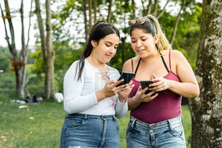 Photo for Girls happily strolling in the park while looking at their cell phones - Royalty Free Image