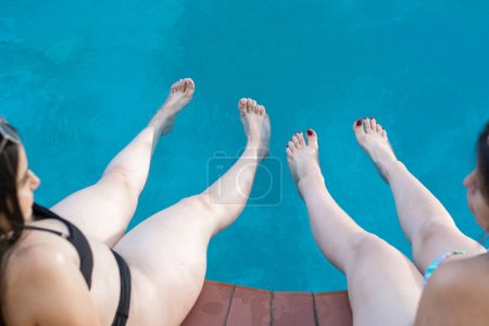 Photo for Zenithal shot of the legs of two latin women getting into the hotel pool, enjoying their trip. - Royalty Free Image