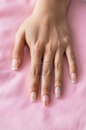 Foto de Vista detallada de la mano de una niña con las uñas decoradas con una manicura tradicional sobre un fondo rosa - Imagen libre de derechos