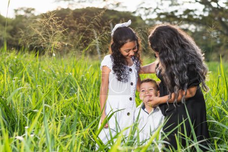 Téléchargez les photos : Famille latine, jeune mère et fille regardant attentivement comme son jeune fils sourit vivement - en image libre de droit