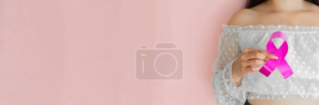 Photo for Close-up of a girl holding a pink ribbon, symbol of breast cancer. on a pink background - Royalty Free Image