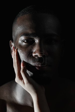 close-up of an African-American man's face with a Caucasian woman's hand on his cheek. 90-degree light.