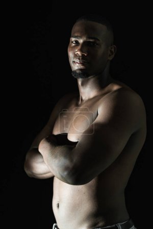 medium shot of a black African-American male posing sideways with his hands folded on a black background