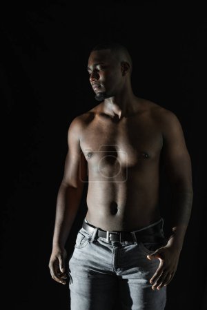 black African-American man posing shirtless on a black background, looking to one side