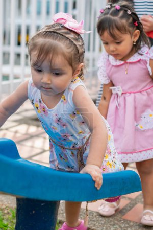 little latina girl climbing on the little slippery slide while another girl waits for her turn