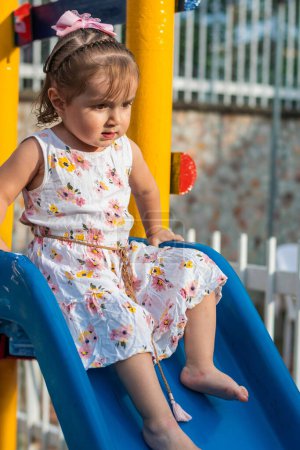 Photo for Little latina girl sitting on the slippery little slide about to slide down the - Royalty Free Image