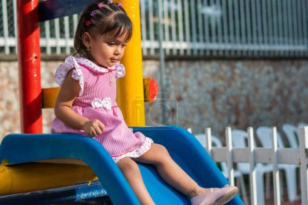 Photo for Little brunette latina girl sitting on top of small slippery slide about to slide down - Royalty Free Image