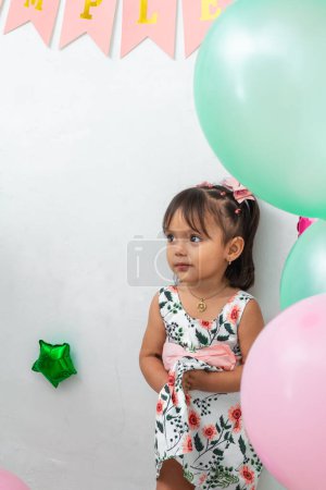 little brunette latina girl clutching her flower dress, surrounded by balloons