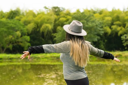 Téléchargez les photos : Latina femme ouvrant ses bras, tout en regardant vers le lac et en admirant la nature. retour - en image libre de droit