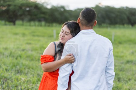 Photo for Young latina woman hugging her boyfriend while leaning on his shoulder. man with his back turned. - Royalty Free Image