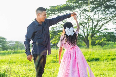 Lateinischer Vater hält seine Tochter an der Hand, um ihr selbstständig einen Wirbel zu geben, während er sie stolz und lächelnd ansieht