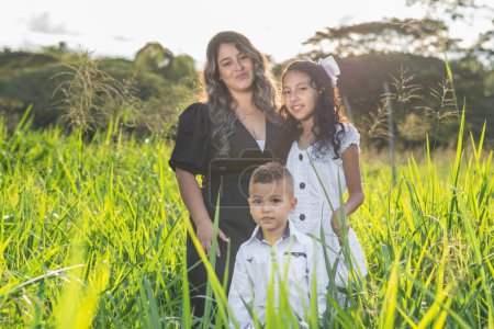 Latino family, single mother posing with her two children in a field of tall grass with a beautiful sunset in the background.