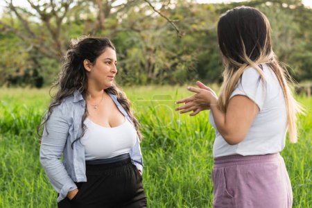 Foto de Dos amigos latinos hablando y discutiendo, mientras dan un paseo por el parque chismorrean sobre sus vidas - Imagen libre de derechos
