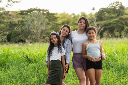 Photo for Two young Latin women posing with their daughters in the middle of a field on a summer day - Royalty Free Image