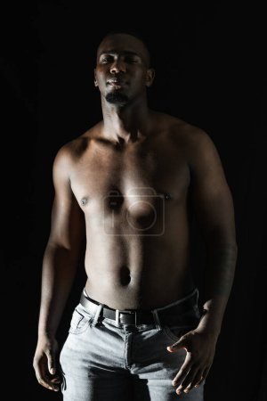 homme noir afro-américain posant torse nu sur un fond noir, regardant droit devant. Éclairage à 90 degrés.