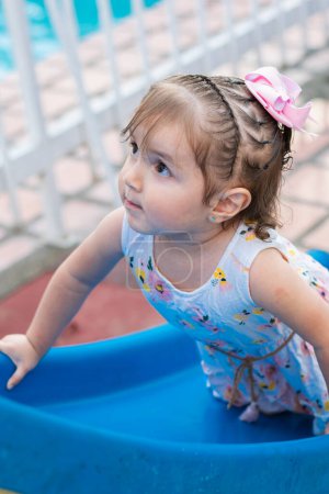 little latina girl climbing on the small slippery slide on the opposite side