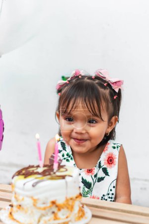 petite fille brune latine très heureuse et souriante tout en regardant son gâteau d'anniversaire