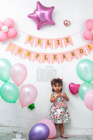 little brunette latina girl celebrating her birthday surrounded by colorful balloons