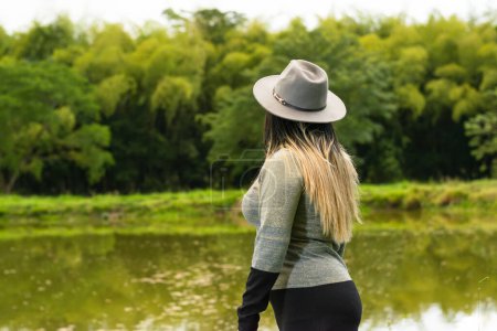 Blick auf den Rücken einer lateinischen Frau, die die Natur bewundert, neben einem See.