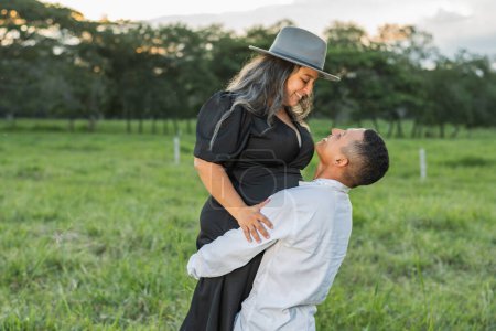 Photo for Young latin couple in love in a field of green grass, man carrying his girlfriend - Royalty Free Image