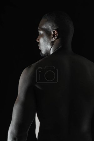close-up of the back of a black African-American man looking out of the corner of his eye, on a black background with 90-degree lighting.