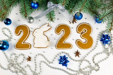 Foto de Tarjeta de felicitación 2023. Números de conejo y pan de jengibre. Decoración en forma de ramas de abeto y bolas azules - Imagen libre de derechos