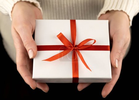 Photo for Small white gift box with red ribbon in beautiful female hands - Royalty Free Image