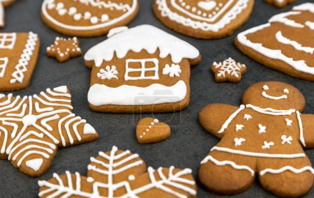 Téléchargez les photos : Biscuits au pain d'épice de Noël avec glaçage sur un fond gris en forme de maison et un homme de pain d'épice, un arbre de Noël et des boules, des étoiles et des flocons de neige et des cœurs. Gros plan - en image libre de droit