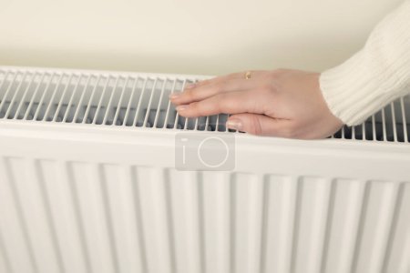 Téléchargez les photos : The concept of the heating season. A womans hand tries to check whether the heating radiator is warm - en image libre de droit