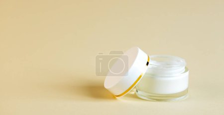 Foto de Frasco de vidrio redondo abierto con crema cosmética y tapa al lado, sobre un fondo beige. Concepto de cuidado de la piel - Imagen libre de derechos