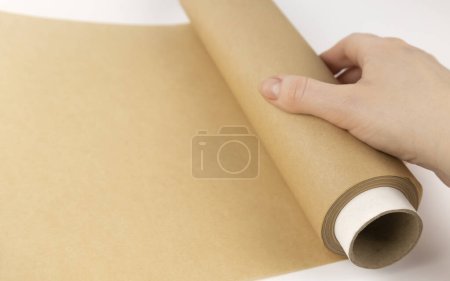 Téléchargez les photos : Déroulement d'un rouleau de papier parchemin. Une main de femme déroule du papier à pâtisserie. Le concept de cuisson - en image libre de droit