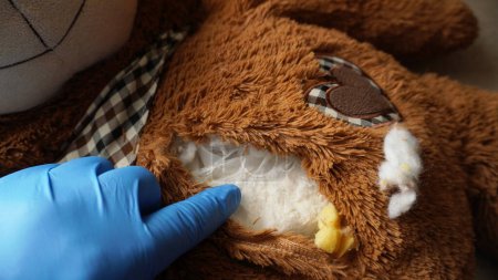 Téléchargez les photos : Un ours en peluche, avec une cachette à l'intérieur, duquel un sac de poudre blanche jaillit - en image libre de droit