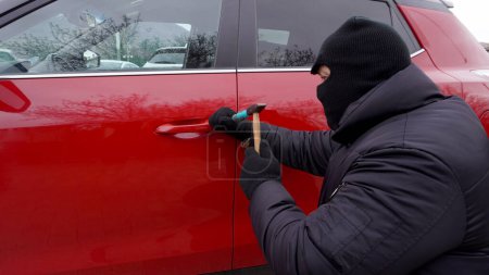 Téléchargez les photos : A thief in a black mask, hacks a car, red color - en image libre de droit