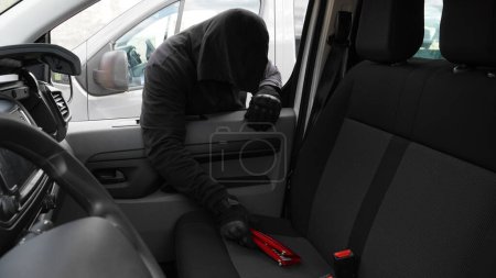 Foto de Un hombre con capucha negra roba una billetera roja de un coche - Imagen libre de derechos