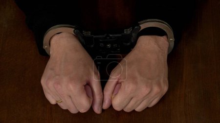 Photo for The hands of a man in handcuffs , on the background of a wooden table . close-up - Royalty Free Image