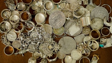   a lot of silver jewelry mixed with silver coins scattered on a wooden table                             