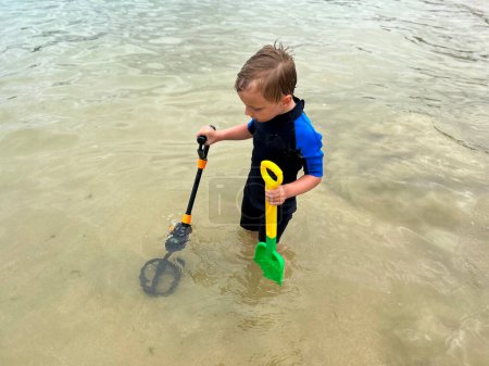 Foto de Un niño buscando tesoros en la playa, con un detector de metales - Imagen libre de derechos