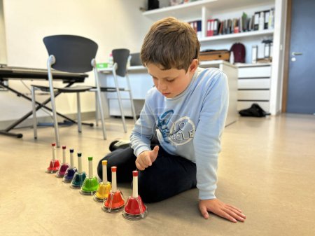 Téléchargez les photos : Garçon jouant des cloches musicales colorées, musicothérapie pour les enfants avec autisme - en image libre de droit