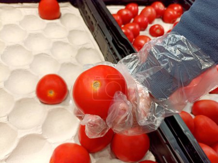 a child's hand in a glove picks tomatoes in a store