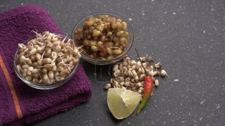 Foto de Close up view of raw and prepared sprouted soy in bowls with towel, lemon and peppers, healthy food concept - Imagen libre de derechos