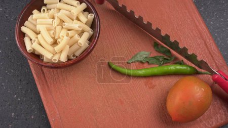 Téléchargez les photos : Pâtes crues fraîches dans un bol en bois avec chili vert, couteau et tomate sur planche à découper marron - en image libre de droit